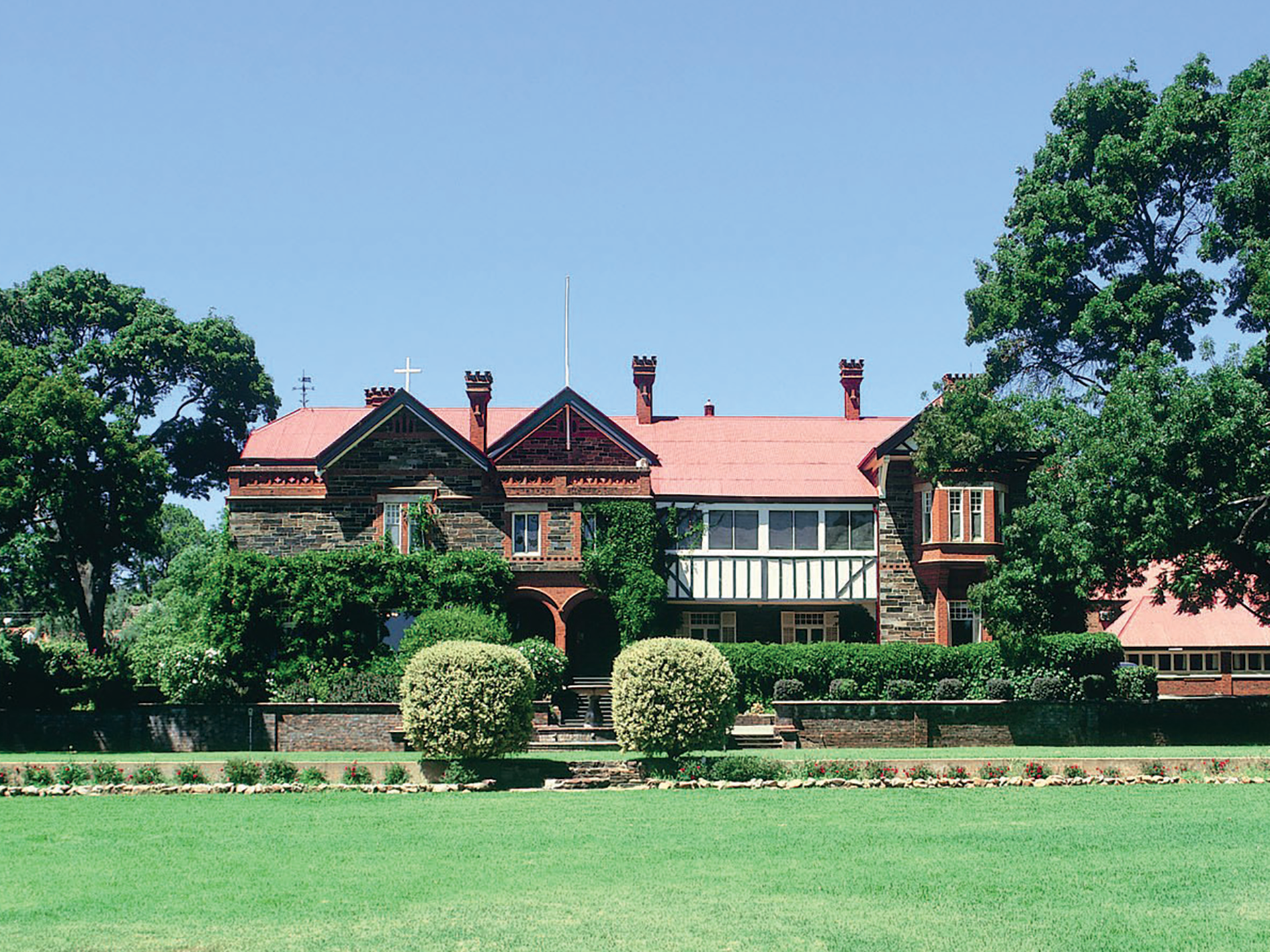 Heritage building at Mercedes College featuring red roof, historic stonework, and manicured gardens.