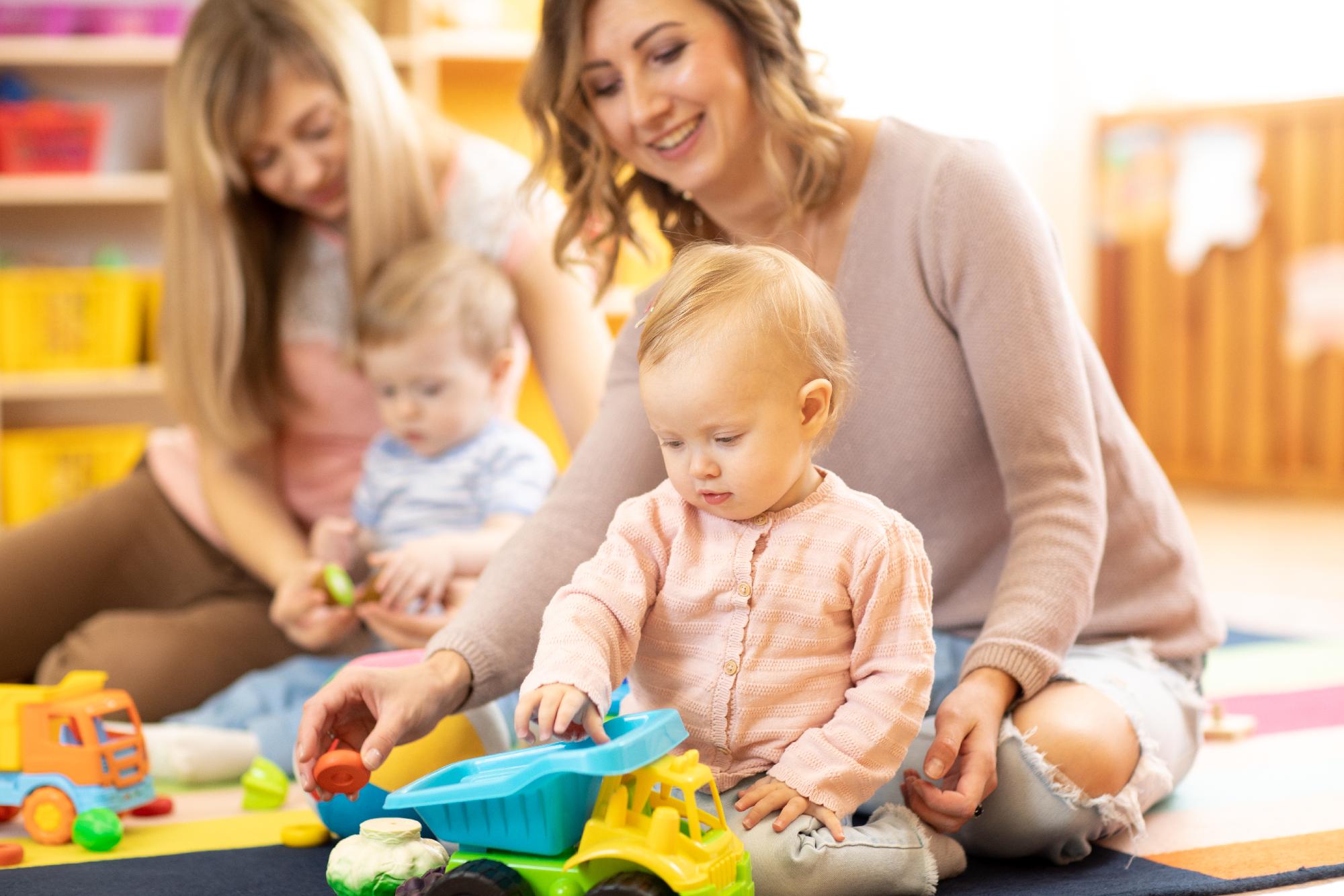 Young child exploring colourful toys with a smiling caregiver at playgroup.