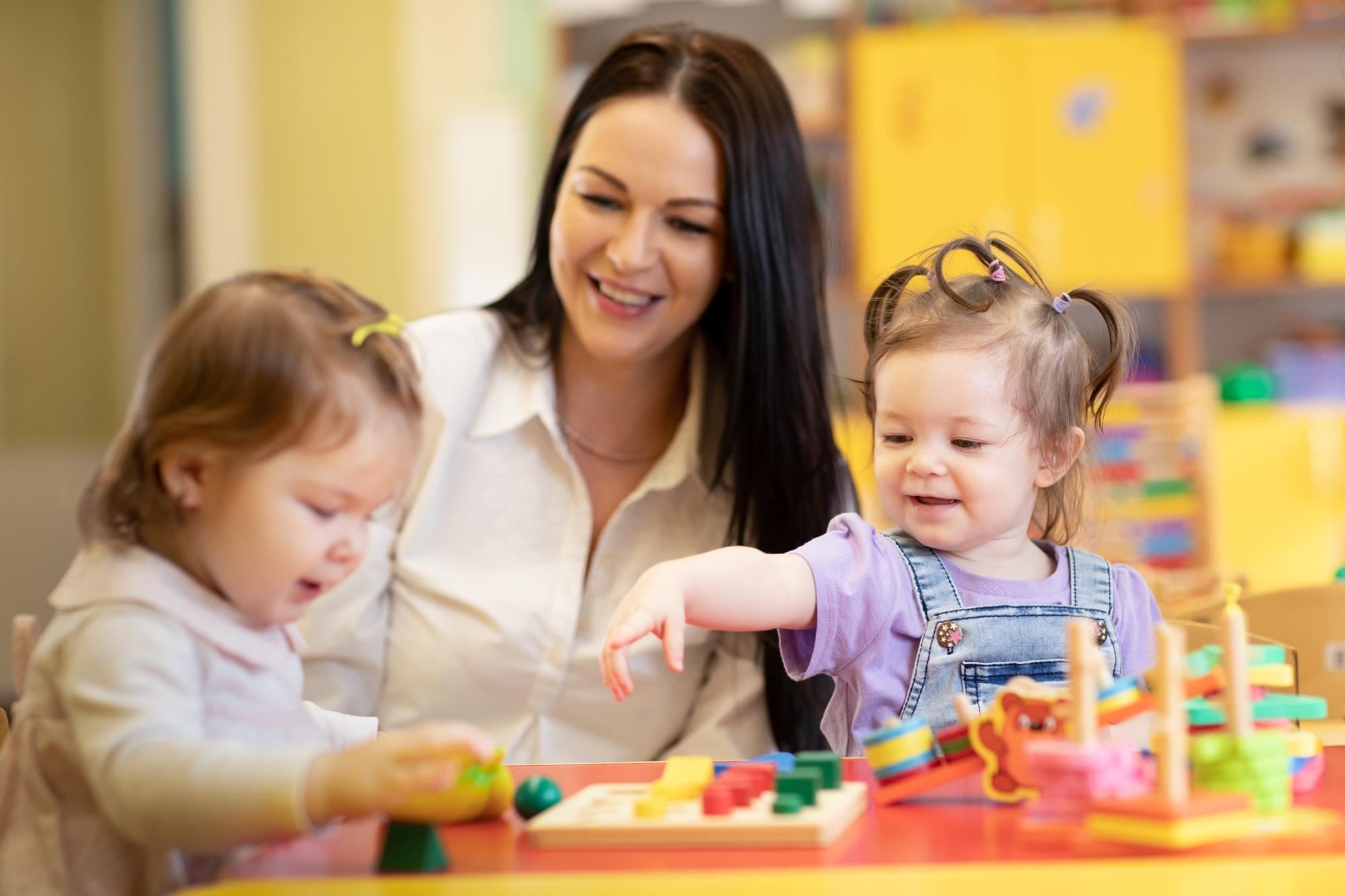 Playgroup educator with two toddlers playing with colourful educational toys.